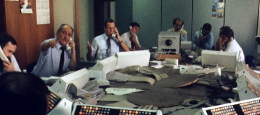 Still uit de documentaire Paradigma. Een groep mannen zit druk telefonerend aan een tafel met monitors.